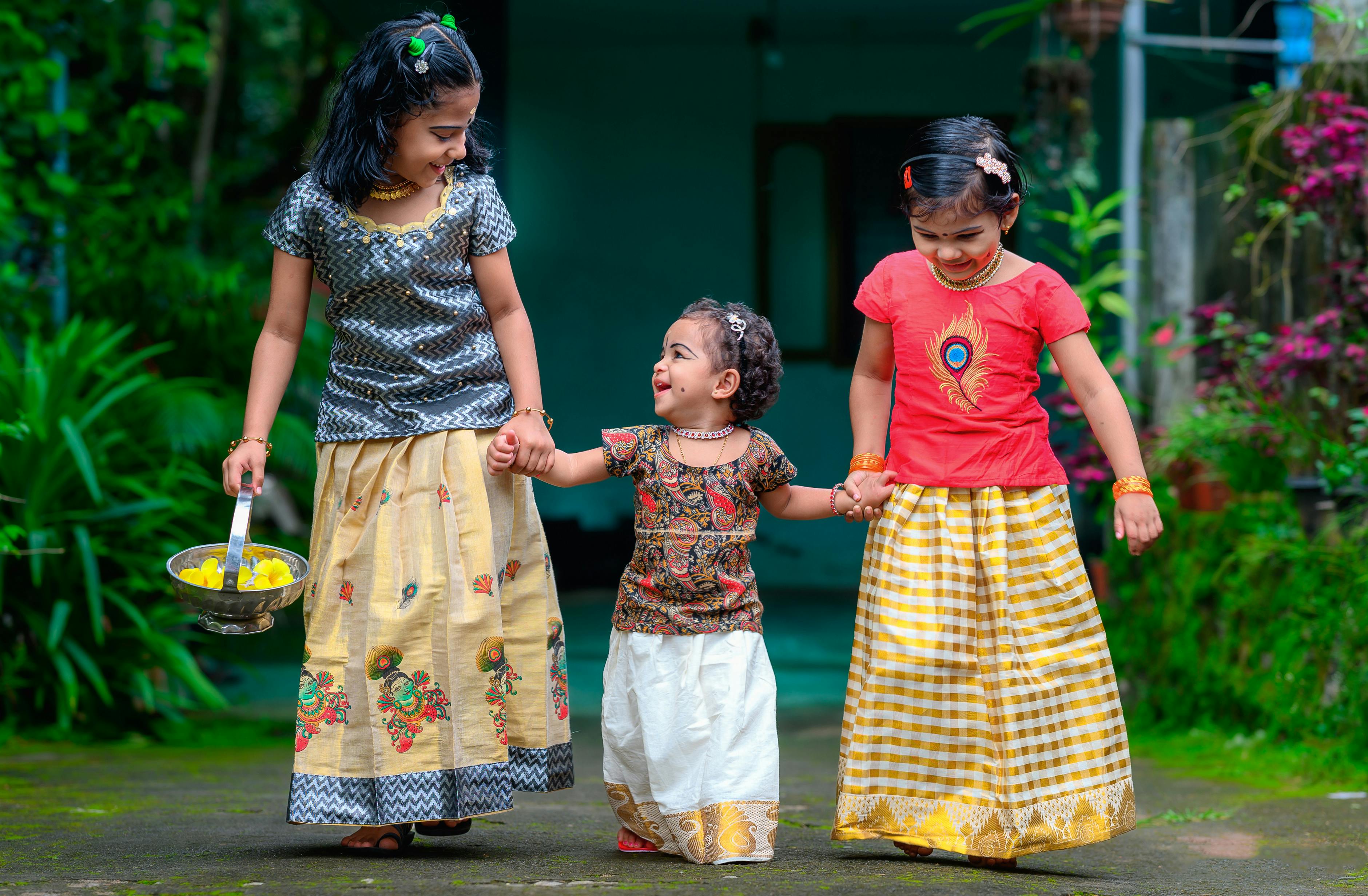 Three children in traditional Kerala attire holding hands and smiling