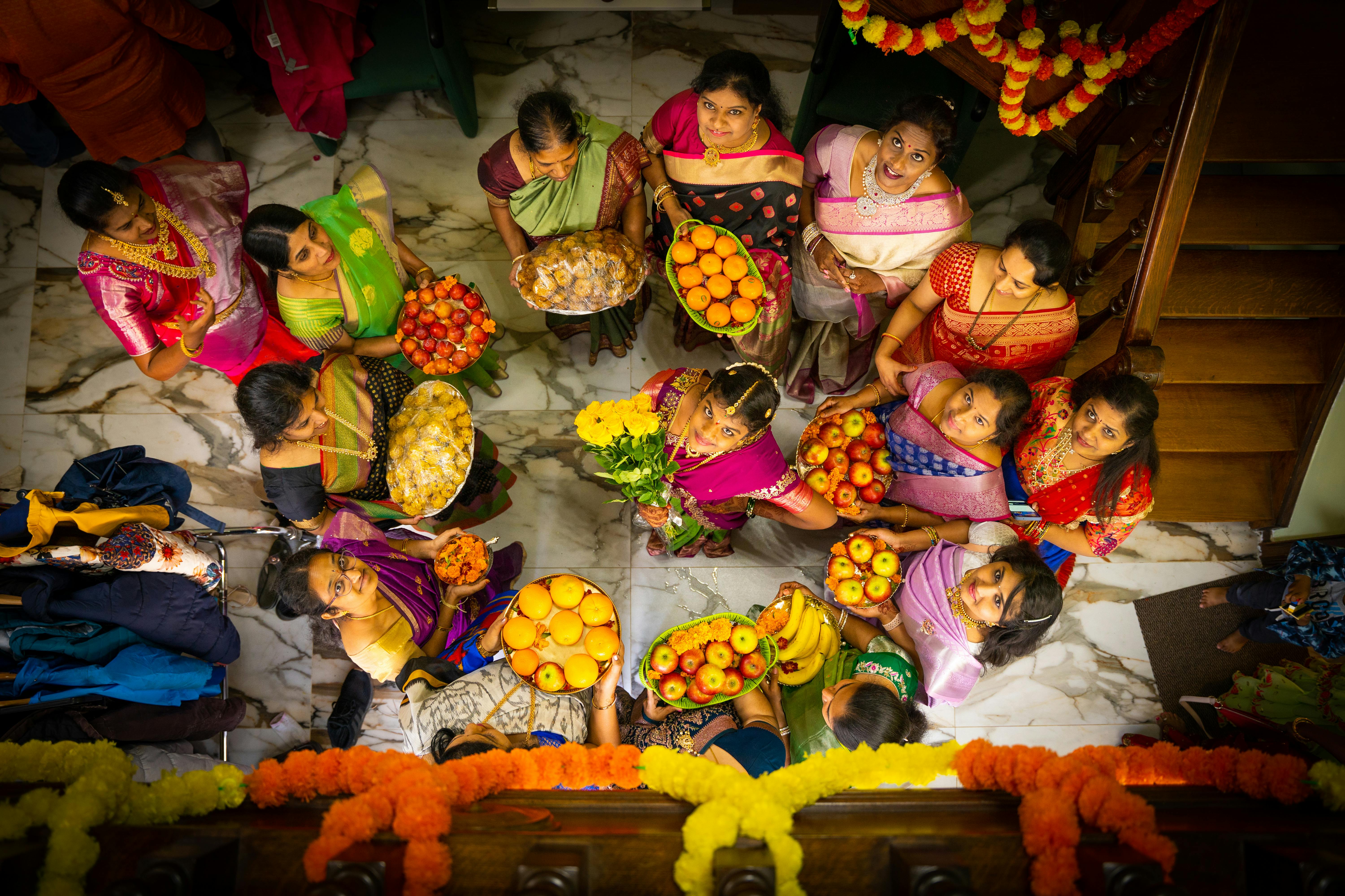 Aerial view of women in sarees carrying flower and fruit offerings
